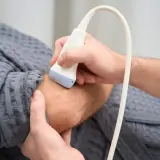 Ortopeda wykonuje badanie USG nadgarstka pacjenta, co jest kluczowe w diagnostyce schorzeń układu ruchu.
