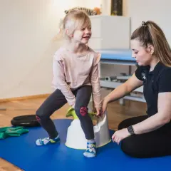 Fizjoterapeutka pomaga dziewczynce ćwiczyć na nocniku. To część poradnika fizjoterapeuty, wspierającego rozwój dziecka.