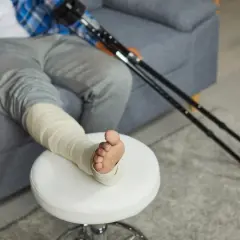 Osoba z zabandażowaną nogą i kulami opiera się o kanapę.