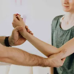 Fizjoterapeuta pomaga w rehabilitacji ręki po złamaniu kości ramiennej, delikatnie masując przedramię pacjentki.