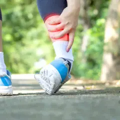 Kobieta trzyma się za bolącą kostkę podczas biegu na zewnątrz.