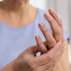 Dłoń z paznokciami pomalowanymi na różowo, osoba masuje palec wskazujący, odczuwając mrowienie.
