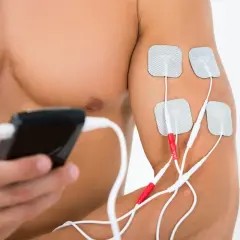 Mężczyzna stosuje elektrostymulację TENS na ramieniu. Elektrody podłączone do urządzenia to element fizjoterapii.