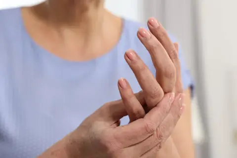 Dłoń z paznokciami pomalowanymi na różowo, osoba masuje palec wskazujący, odczuwając mrowienie.