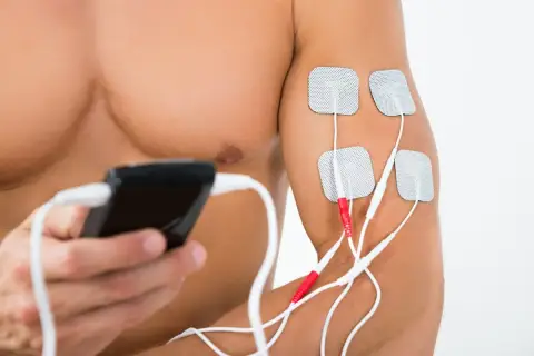 Mężczyzna stosuje elektrostymulację TENS na ramieniu. Elektrody podłączone do urządzenia to element fizjoterapii.