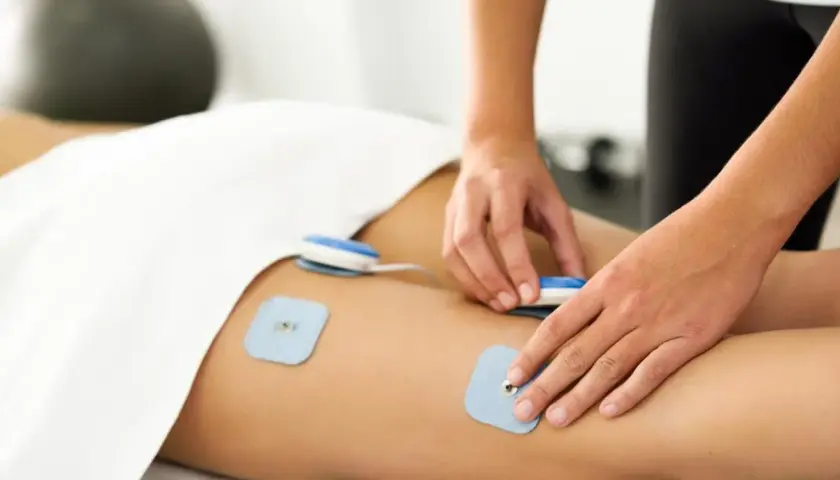 Fizjoterapeuta umieszcza elektrody do elektrostymulacji mięśni na udzie pacjenta.