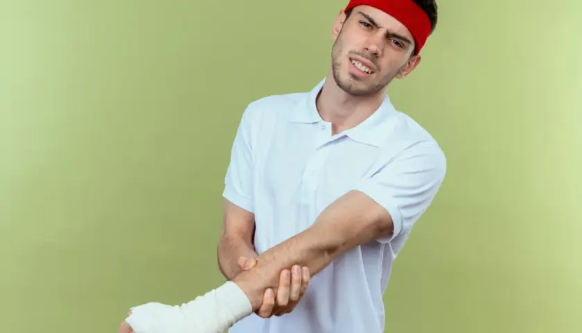 Mężczyzna w czerwonej opasce na głowie i białej koszulce z bólem trzyma rękę w bandażu, jakby po odwróconym teście Cozena.