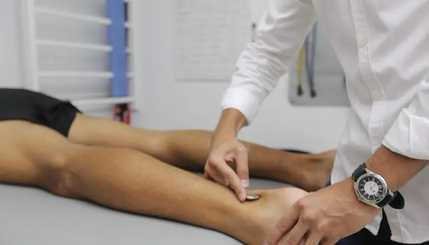 Fizjoterapeuta wykonuje zabieg na stopie pacjenta, co jest częścią rehabilitacji w ramach prewencji rentowej ZUS.