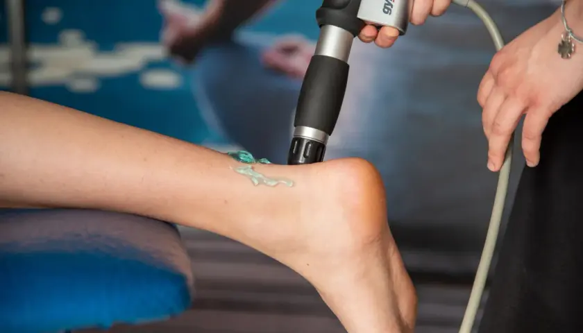 Terapia falą uderzeniową: aplikator z żelem na łydce pacjenta, przygotowanie do zabiegu.
