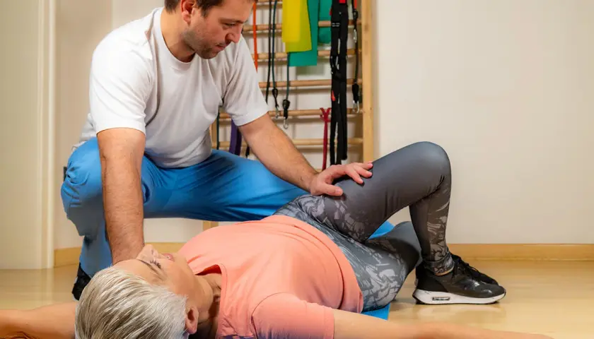 Fizjoterapeuta pomaga pacjentce w ćwiczeniach na macie. Wygodne ubranie, jak legginsy i luźna koszulka, to klucz do komfortu podczas rehabilitacji kręgosłupa lędźwiowego.