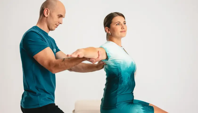 Fizjoterapeuta pomaga pacjentce w ćwiczeniach ramion, kluczowych dla rehabilitacji po złamaniu nadgarstka.