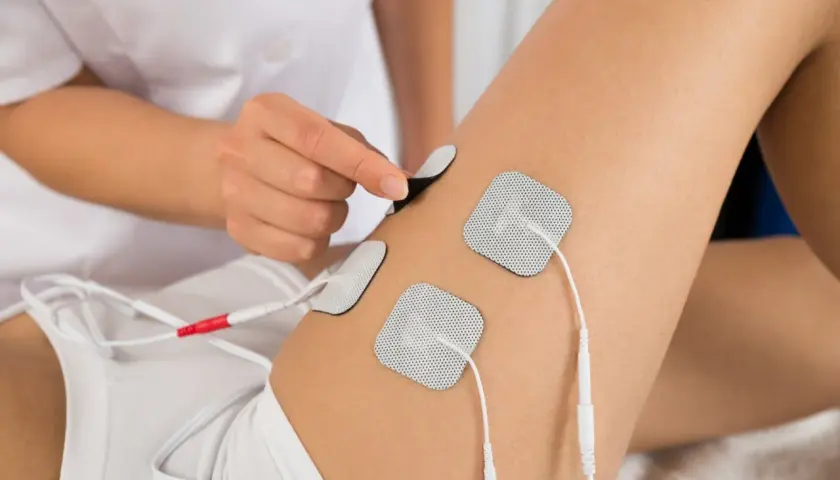 Elektrostymulacja efekty uda: terapeuta umieszcza elektrody na udzie pacjentki, przygotowując do zabiegu.