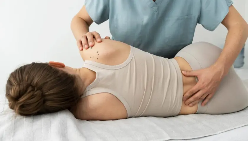 Fizjoterapeuta bada odcinek lędźwiowy pacjentki, która leży na boku. Może to być pomocne przy diagnozowaniu dyskopatii lędźwiowej.