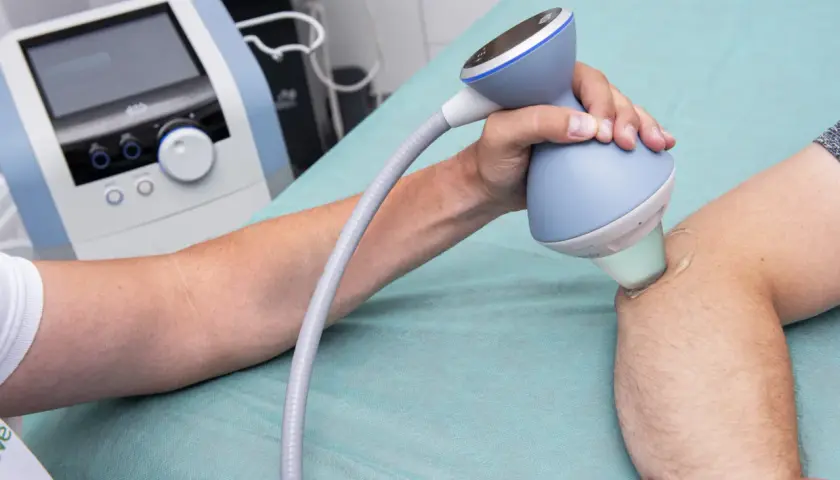 Terapia falą uderzeniową na łokieć tenisisty. Fizjoterapeuta aplikuje żel i głowicę aparatu na bolące miejsce.