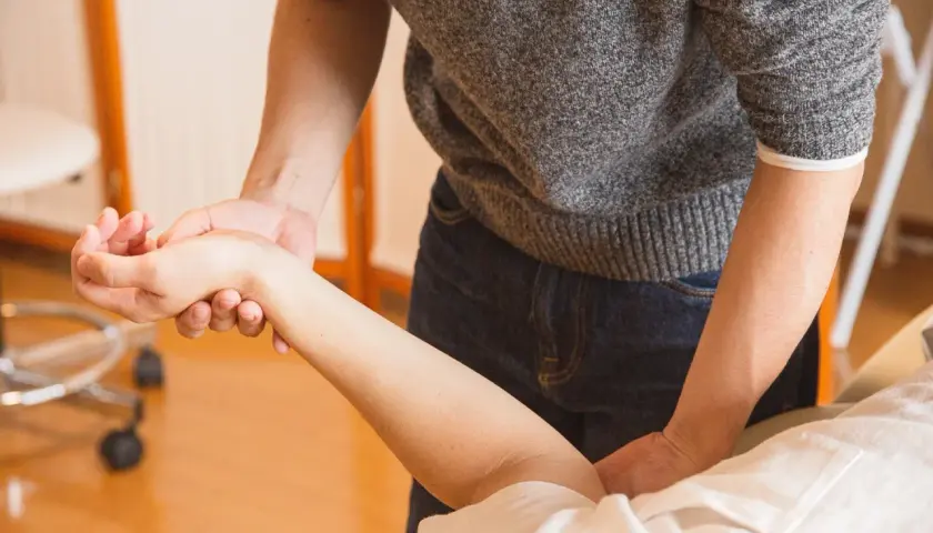Fizjoterapeuta bada rękę pacjenta z problemem braku czucia w palcach po operacji cieśni nadgarstka.
