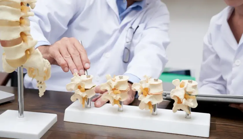 Lekarz pokazuje modele kręgów lędźwiowych z implantami, ilustrując stabilizację kręgosłupa lędźwiowego śrubami.