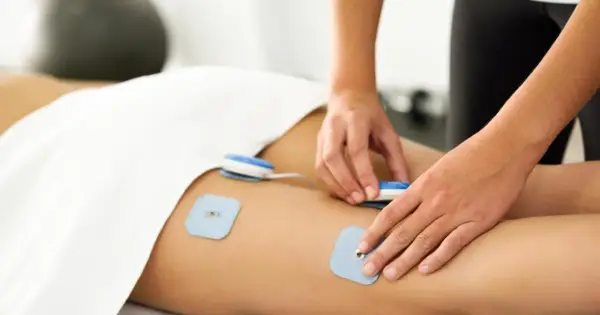 Fizjoterapeuta umieszcza elektrody do elektrostymulacji mięśni na udzie pacjenta.